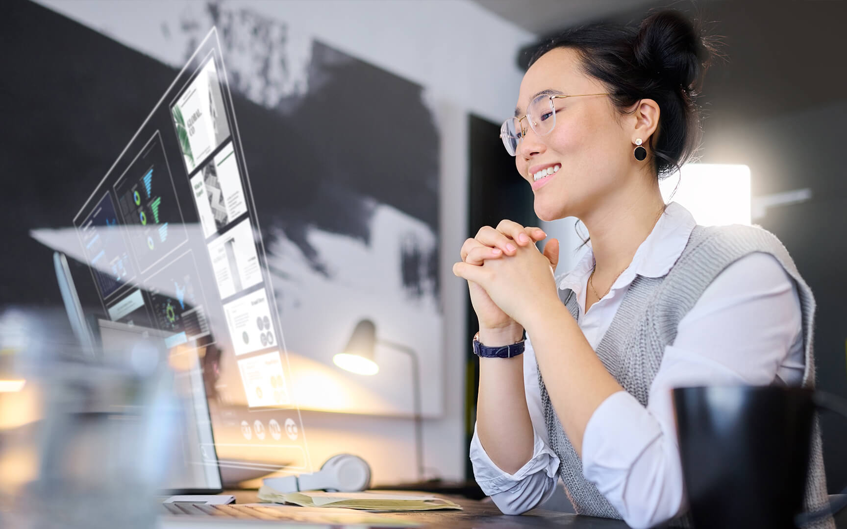A woman smiling while sitting at a desk with a computer screen displaying charts and graphs. 