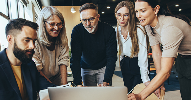 A group of five people gathered around a laptop, discussing ideas in an office setting