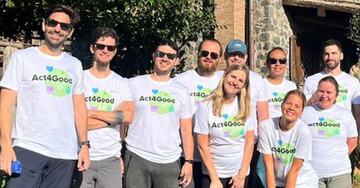 Group of nine people outdoors, wearing matching white t-shirts with 'Act4Good' printed on them, posing together in two rows.