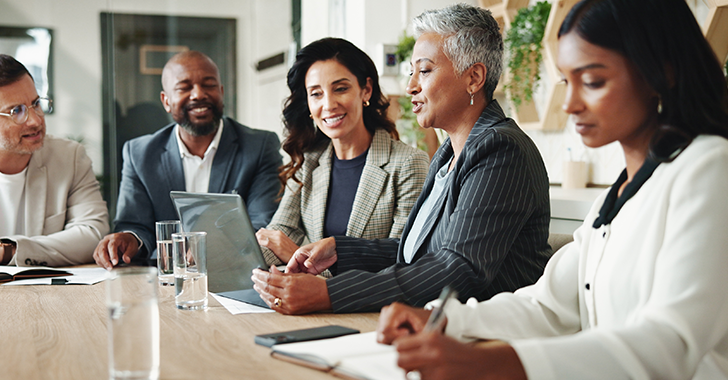 Five professionals seated around a table in a modern office, engaged in a collaborative discussion. 