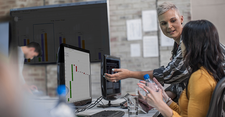 Two professionals in an office setting collaborate in front of desktop monitors
