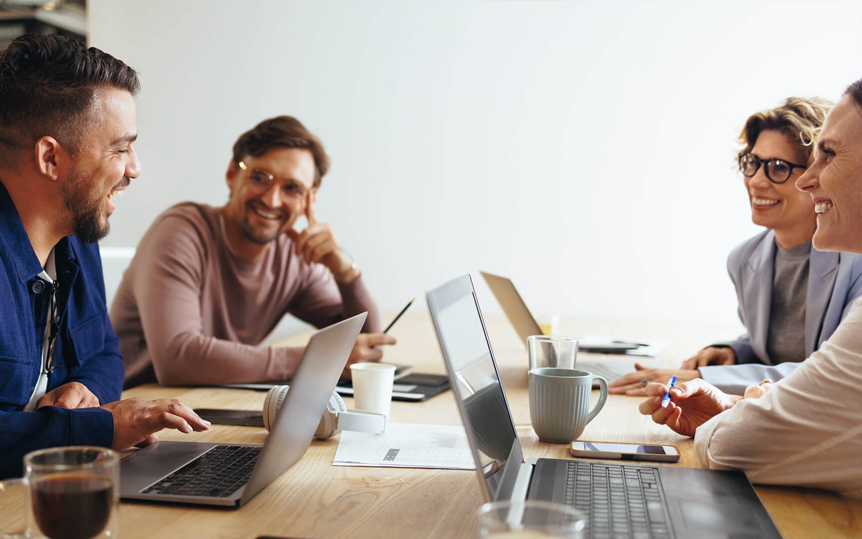 Five individuals gathered around a light wooden table in a modern office setting, engaged in a collaborative discussion. 