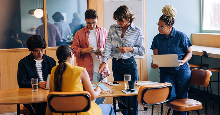 Five individuals gathered around a wooden table in a modern office setting.