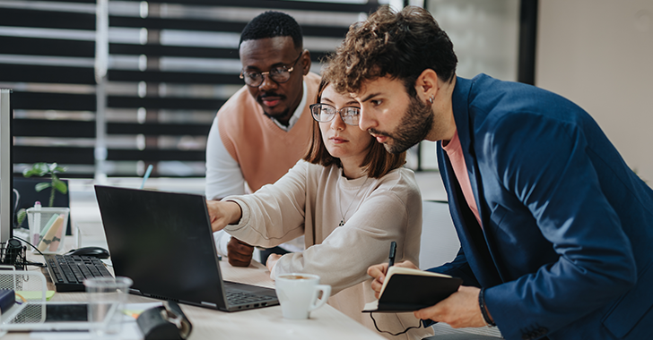 Three colleagues collaborating around a laptop in a bright, modern office setting.