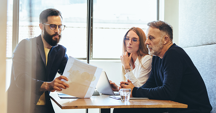 Three individuals seated around a wooden table in a professional setting, engaged in a collaborative discussion.