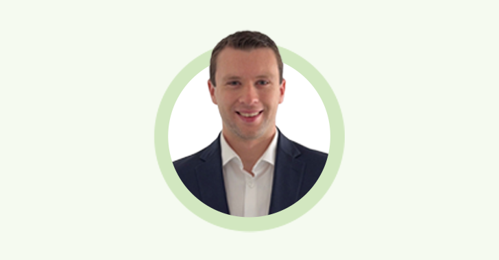 A professional headshot of a smiling man with short brown hair, wearing a dark suit jacket and white collared shirt. 
