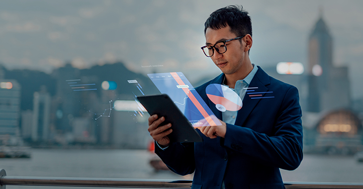 An Asian man in a dark blue suit interacts with a holographic display projected from a tablet.