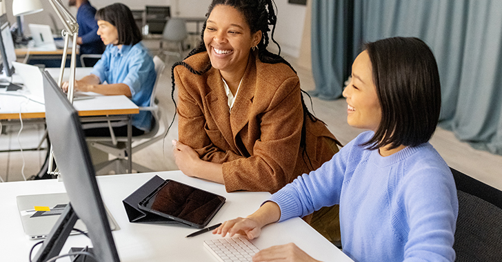 Two women collaborate at a desk in a bright, modern office.