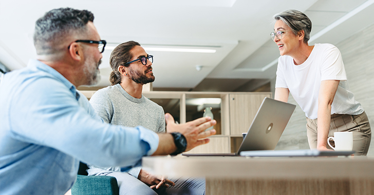 Three colleagues collaborate around a light-colored table in a modern office.