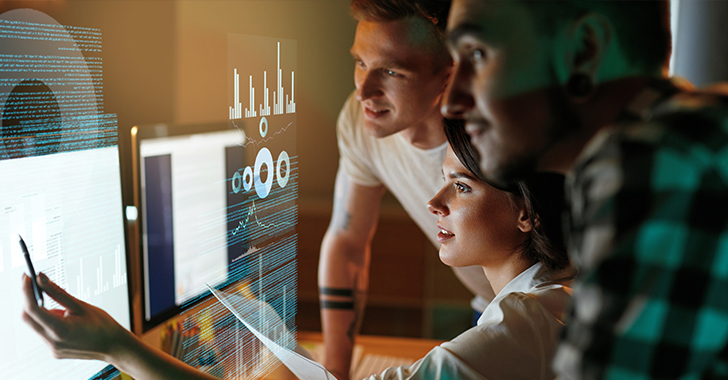 Three professionals collaborate in a dimly lit, high-tech workspace.