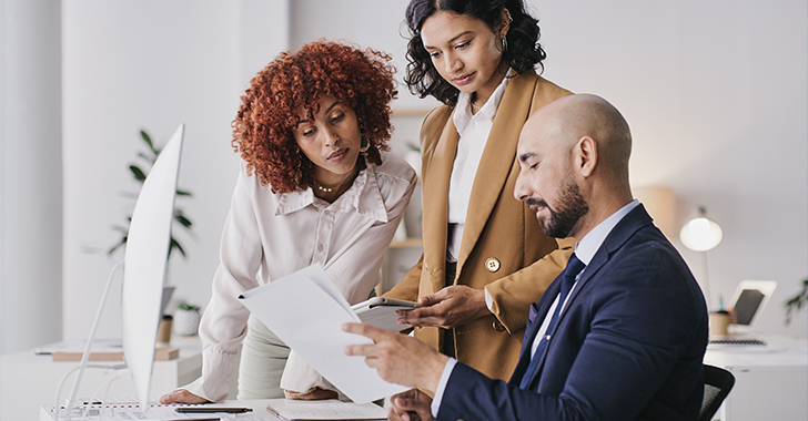 Three professionals collaborate around a light-colored desk in a modern office.