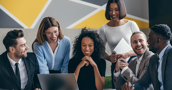 Six diverse professionals collaborate around a laptop in a modern office. 