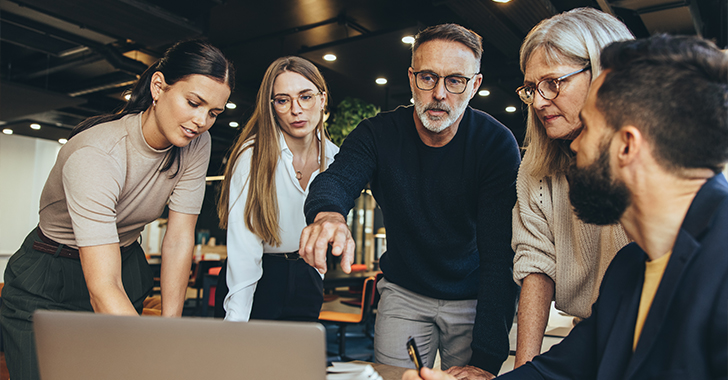 Five professionals collaborate around a table in a modern office.