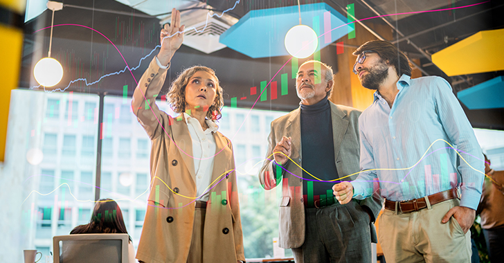 Three professionals in a meeting discussing graphs and data on a screen.