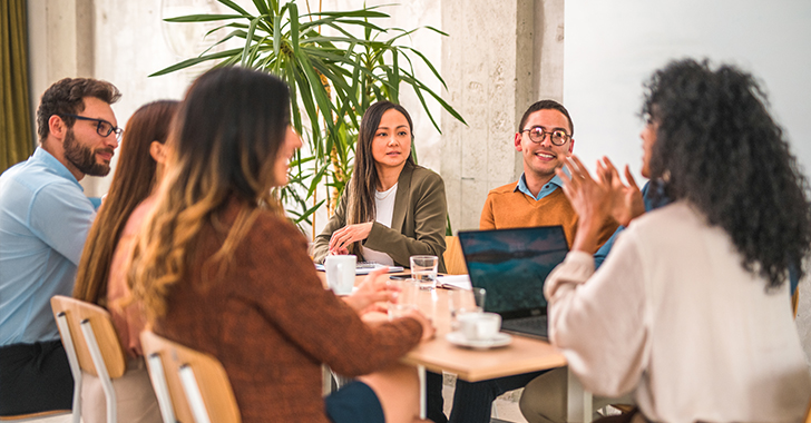 Six professionals collaborate around a light-colored table in a modern office. 