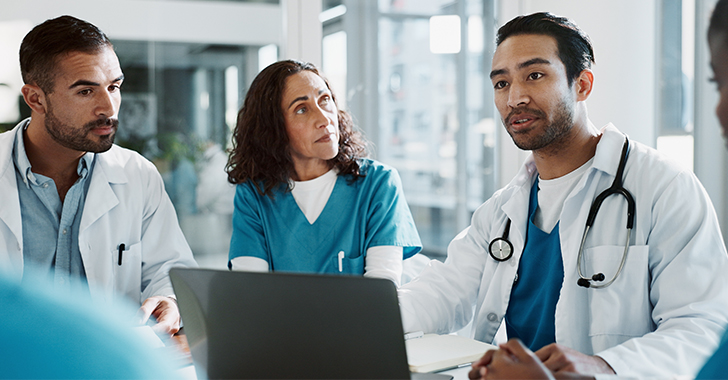 A group of medical professionals discussing in front of a laptop in a bright room