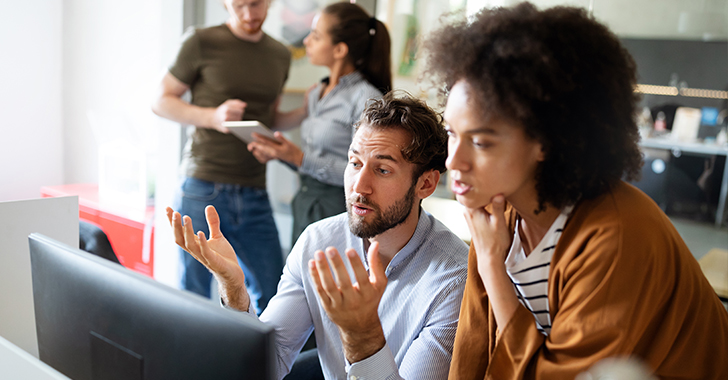 A man and a woman collaborate in a modern office, focused on a computer monitor. 