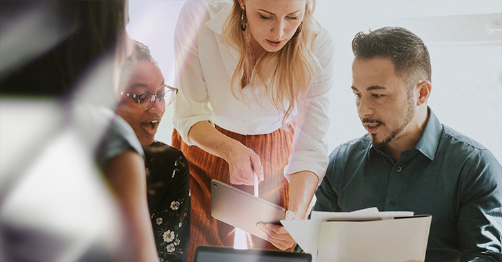 A group of three people engaged in a discussion, one showing a tablet to others. 