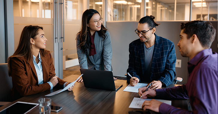 Four colleagues collaborate around a dark wooden table in a modern office. 