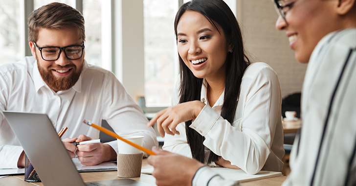 Three people collaborating at a table with a laptop, notebook, and coffee. 