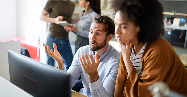 A man and woman discussing something on a computer screen in a busy office. 