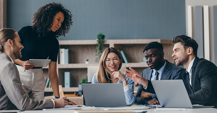 A diverse group of professionals discussing ideas around a laptop in a modern office. 