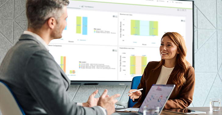 A woman and a man in a meeting discussing charts and data displayed on a screen. 