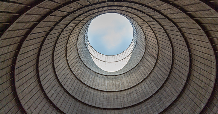 View looking upward through a series of concentric circular concrete rings forming an industrial structure, with an open circular skylight at the top revealing a patch of blue sky. 
