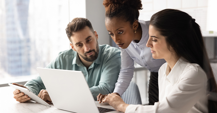 Three people working together at a laptop in an office, focused on the screen. 
