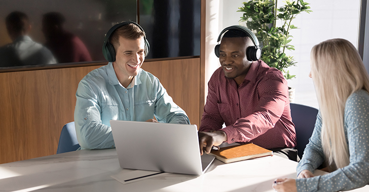 Three colleagues sit around a table in a modern office, collaborating during a video or online meeting. 