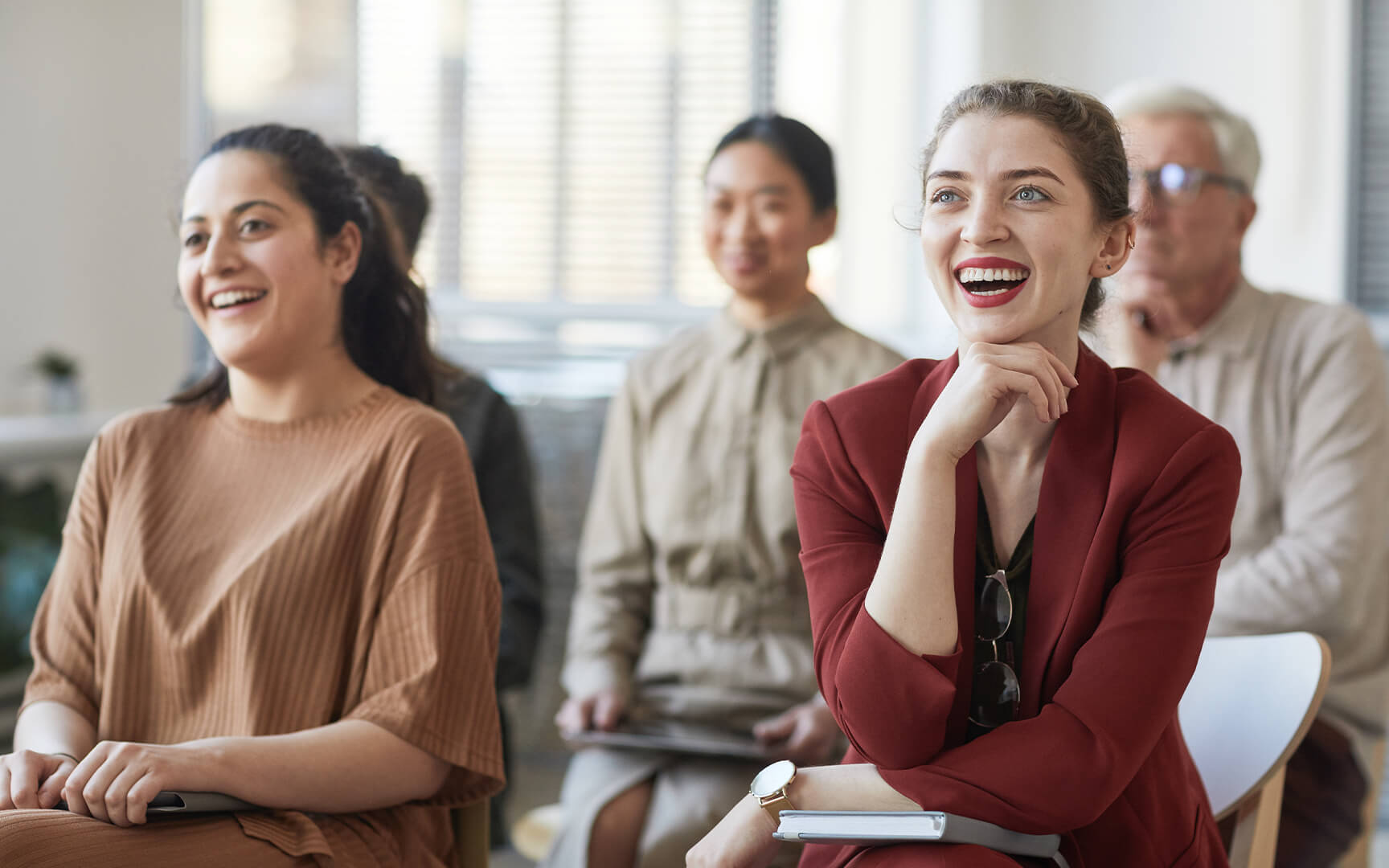 Eine Gruppe von Fachleuten sitzt in einem Meeting oder Seminar, hört aufmerksam zu und macht sich Notizen in einem hellen, modernen Raum.