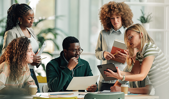 A diverse group of professionals collaborating around a table in a modern office, reviewing documents, a laptop, and a smartphone, with notebooks and coffee cups visible, illustrating teamwork, data analysis, and business decision-making.