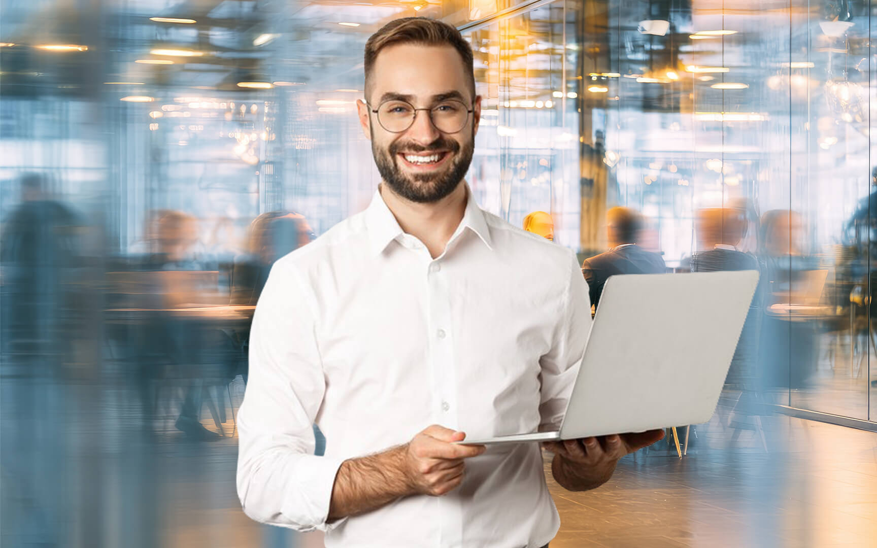 Smiling professional holding a laptop in a modern office environment with blurred colleagues working in the background