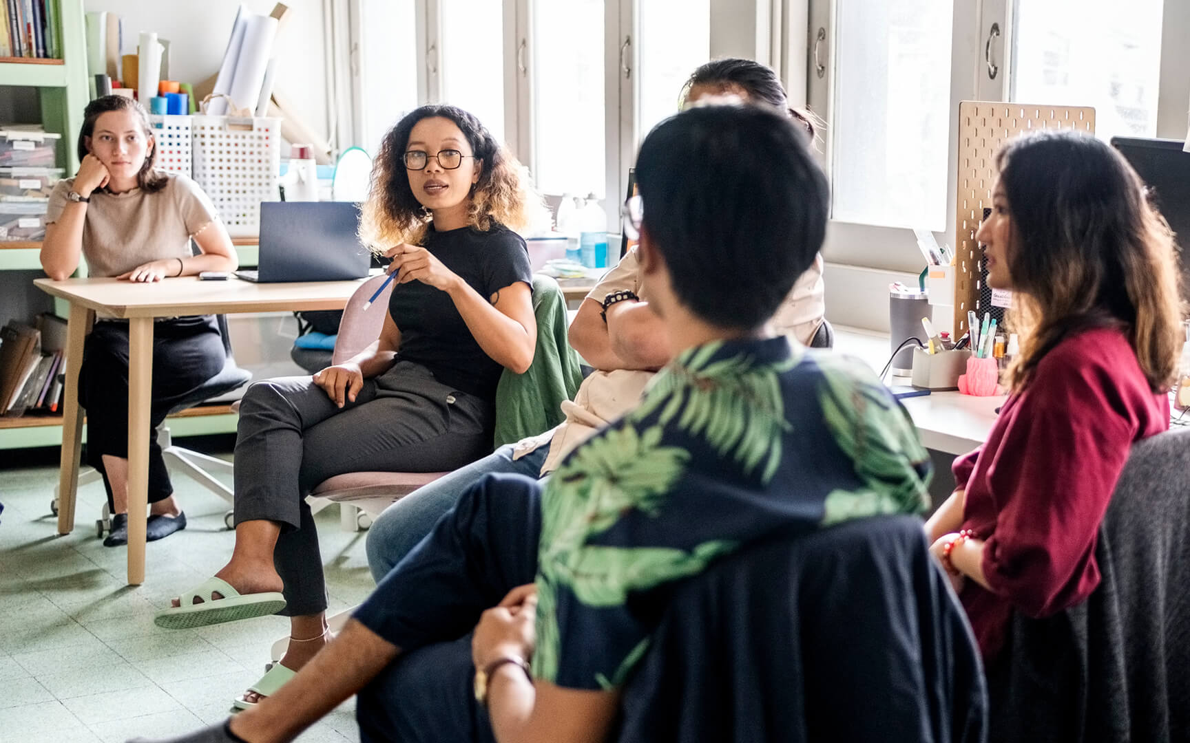 Team discussion in a bright office, with several people seated in a circle while one person speaks and others listen.