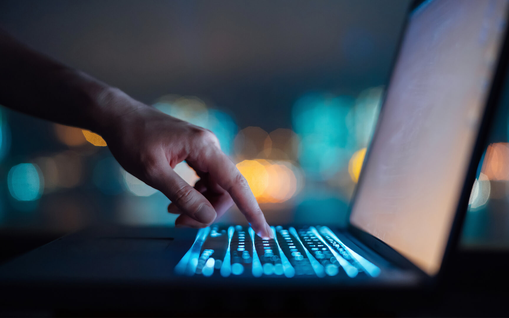 Close-up of a hand typing on a laptop keyboard with glowing blue keys in a low-light setting, representing data analysis or AI-driven work.