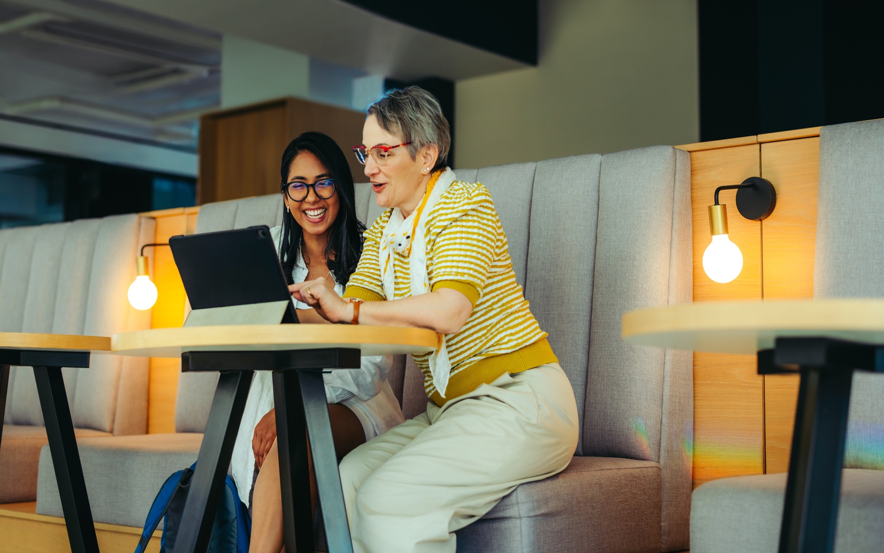 Two professionals collaborate at a tablet while seated in a modern office lounge area. 