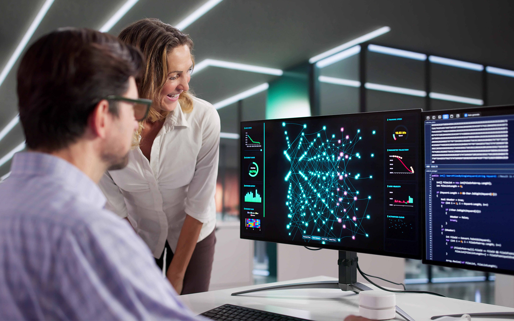 Two professionals review workforce and organizational data on dual computer monitors in a modern office.