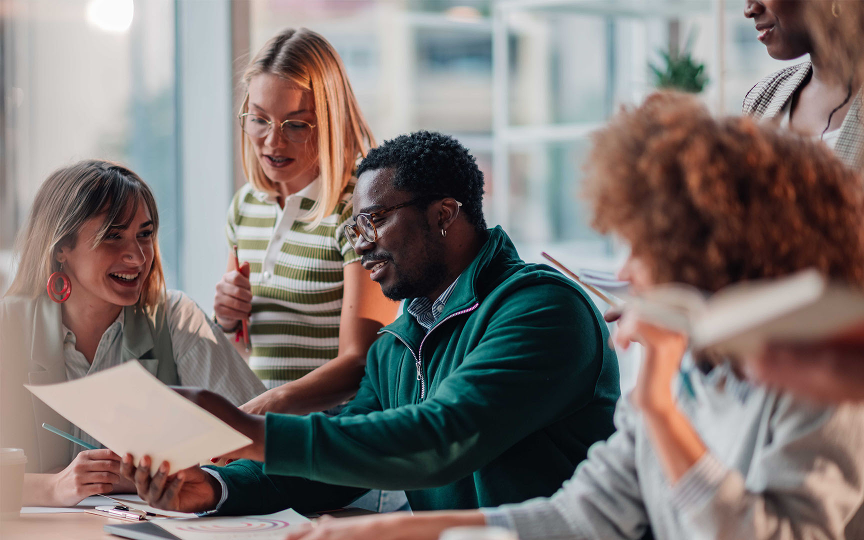 A group of colleagues collaborating around a table in a modern office, reviewing printed documents and discussing ideas during a team meeting.