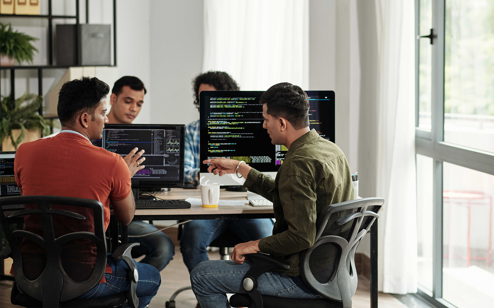 Team members collaborating in a modern office, reviewing code and data dashboards displayed on multiple computer monitors during a software development or technology planning session.