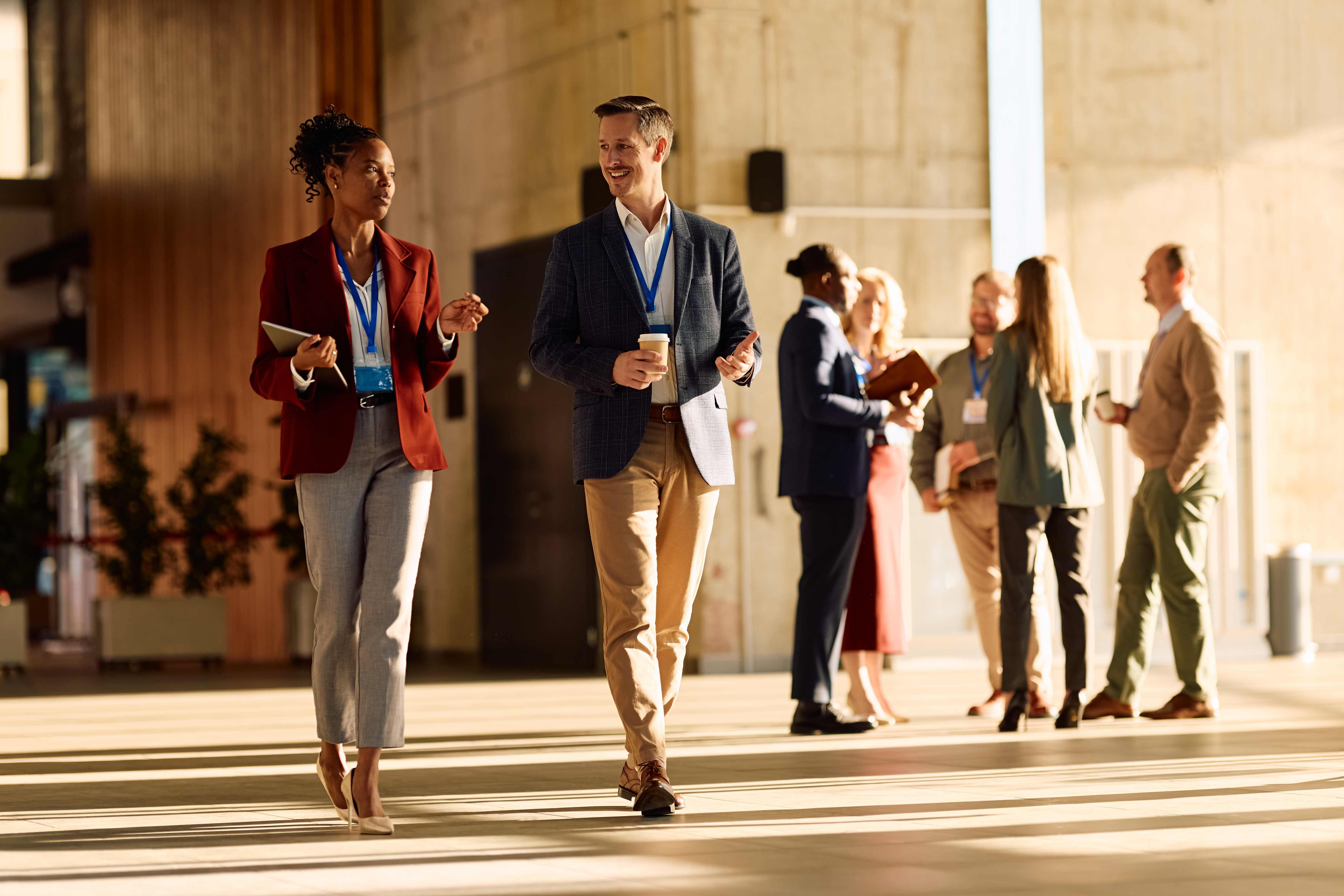 Business professionals wearing conference badges walk and network in a modern event venue.