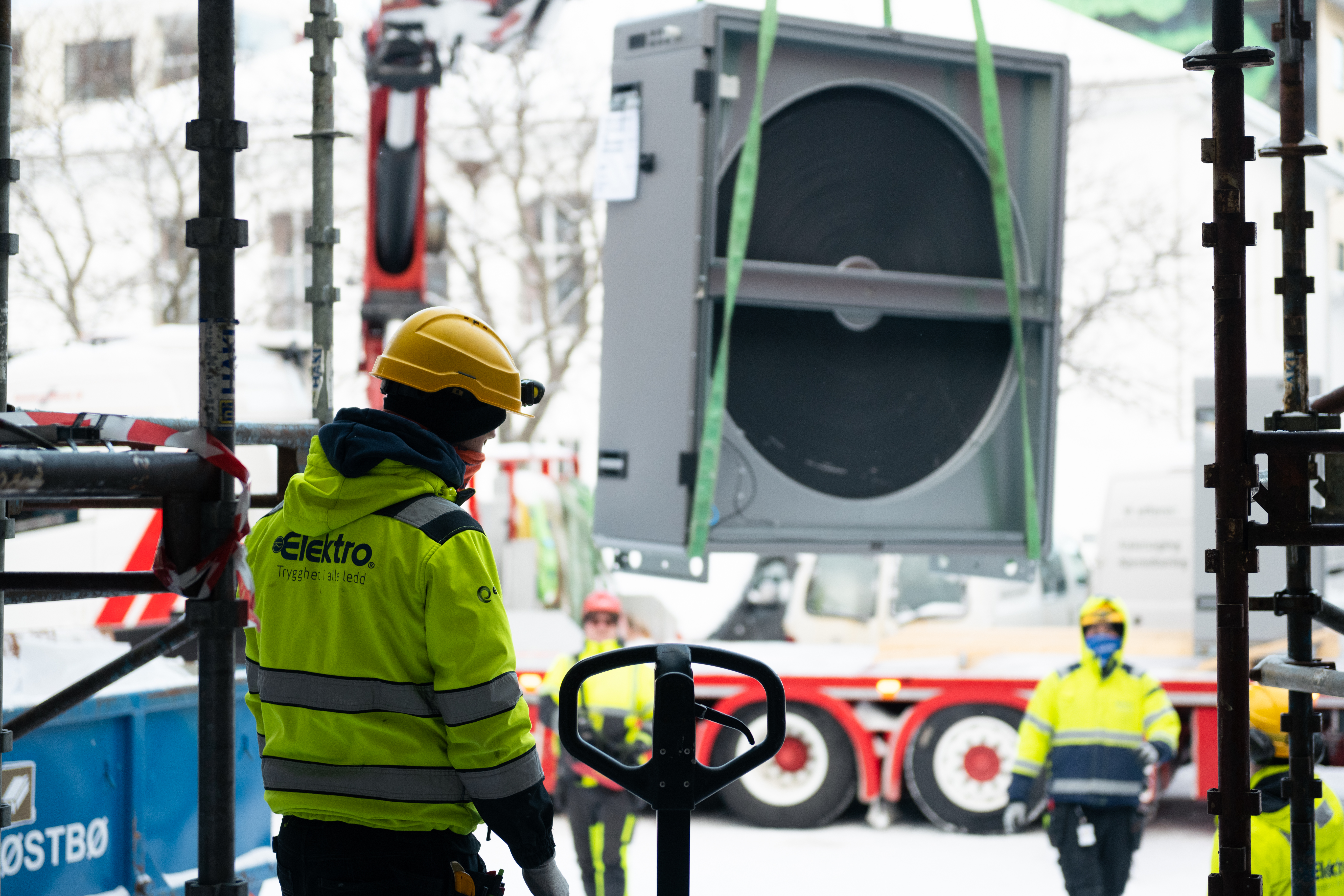 Man with a hardhat and a yellow coat with Elektrogruppen logo on the back on a buliding site