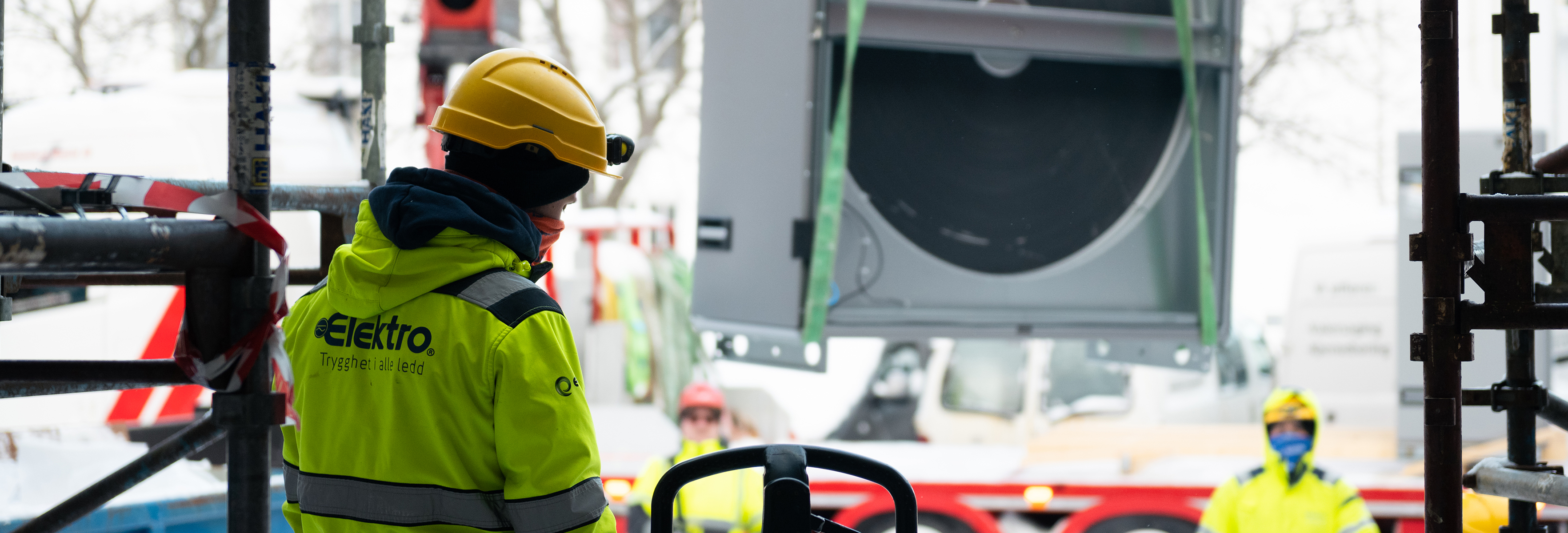 Man with a hardhat and a yellow coat with Elektrogruppen logo on the back on a buliding site