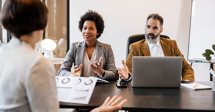 Two business people in suits listening to a presenter in a meeting room.