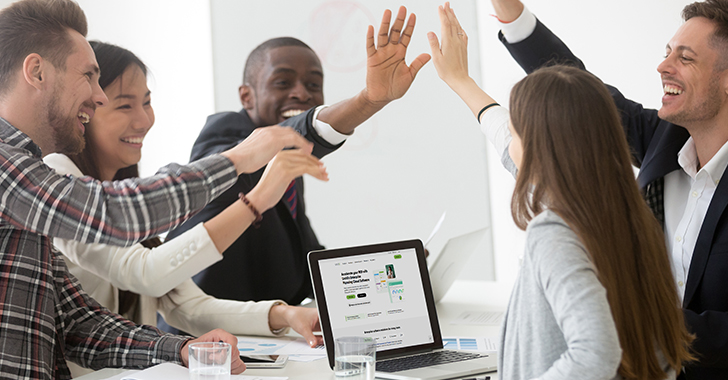 A group of professionals celebrating a successful meeting around a conference table with a laptop displaying a presentation on it.