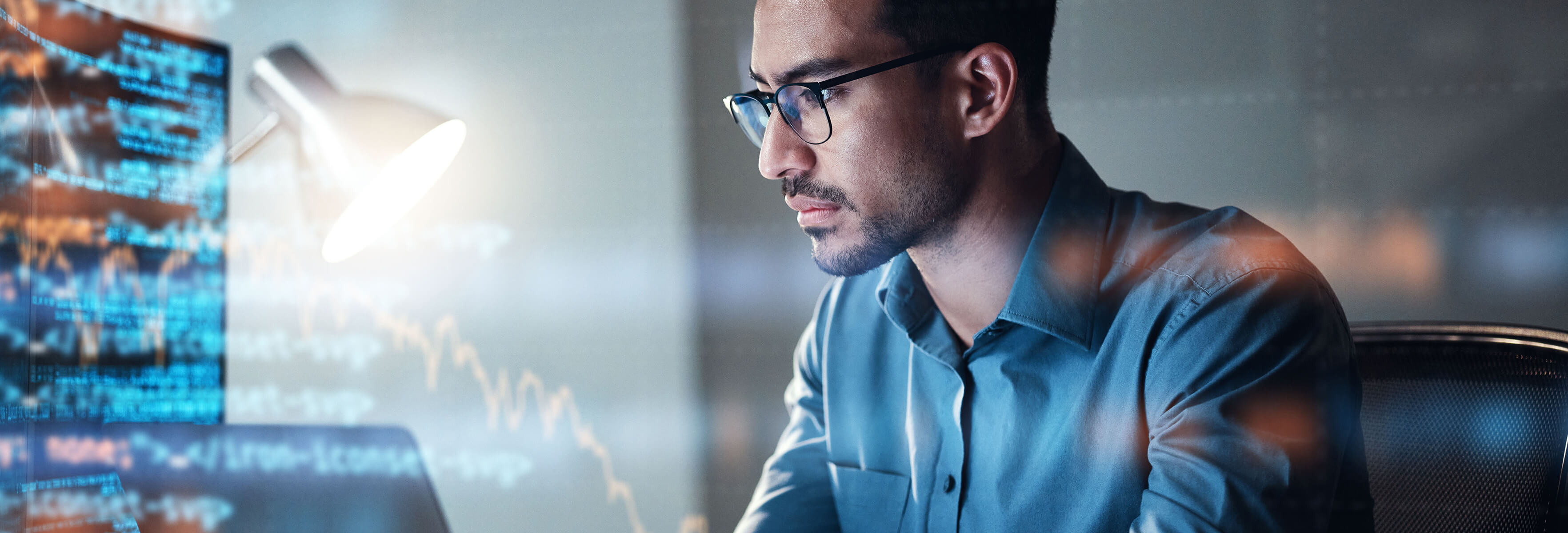 Ammattilainen työskentelee tarkkaavaisesti tietokoneella, jonka näytölle heijastetaan useita koodirivejä hämärässä toimistossa.