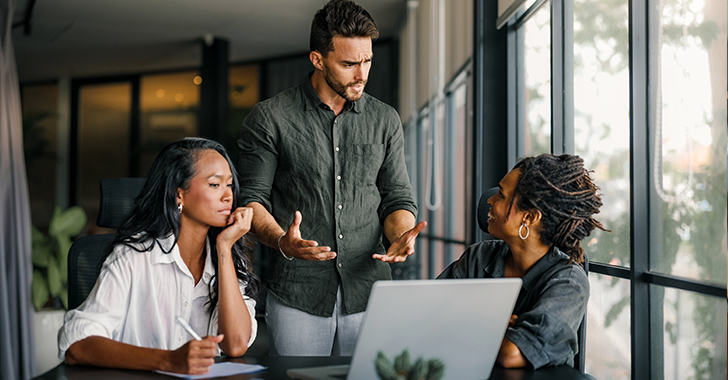 Three professionals in a discussion around a laptop in a modern office setting.