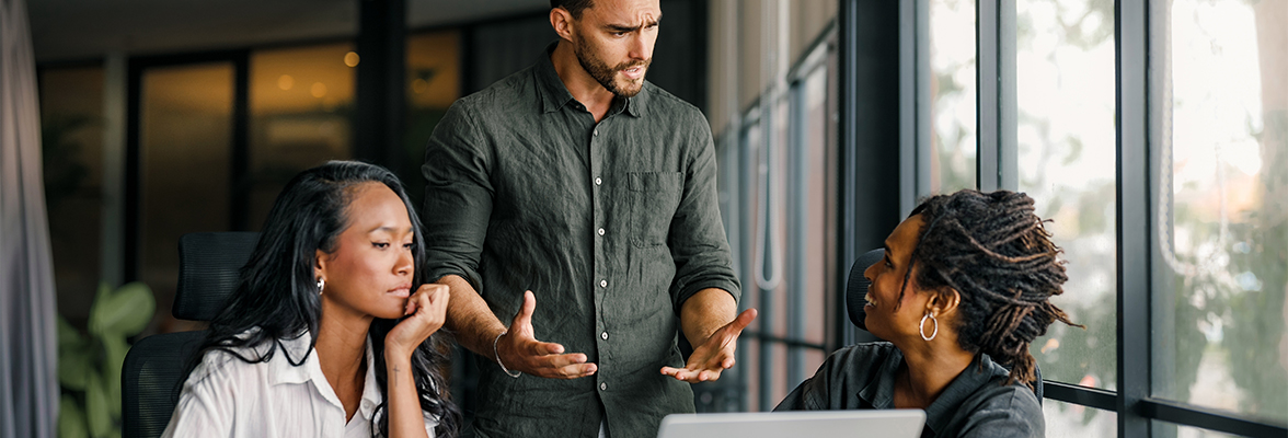 Three professionals in a discussion around a laptop in a modern office setting.