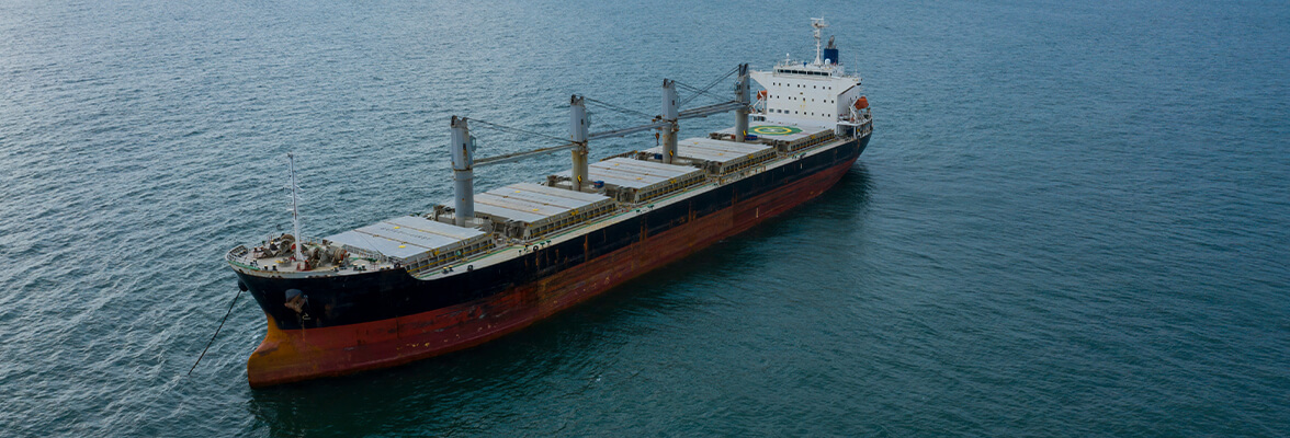 A large cargo ship sails on a vast, calm sea under a cloudy sky.