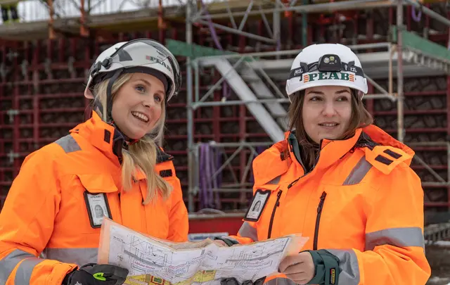 Two women in working clothes with Peab logo and hard hat on a building site