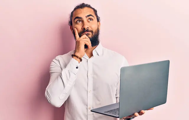 Bearded man thinking and holding a computer